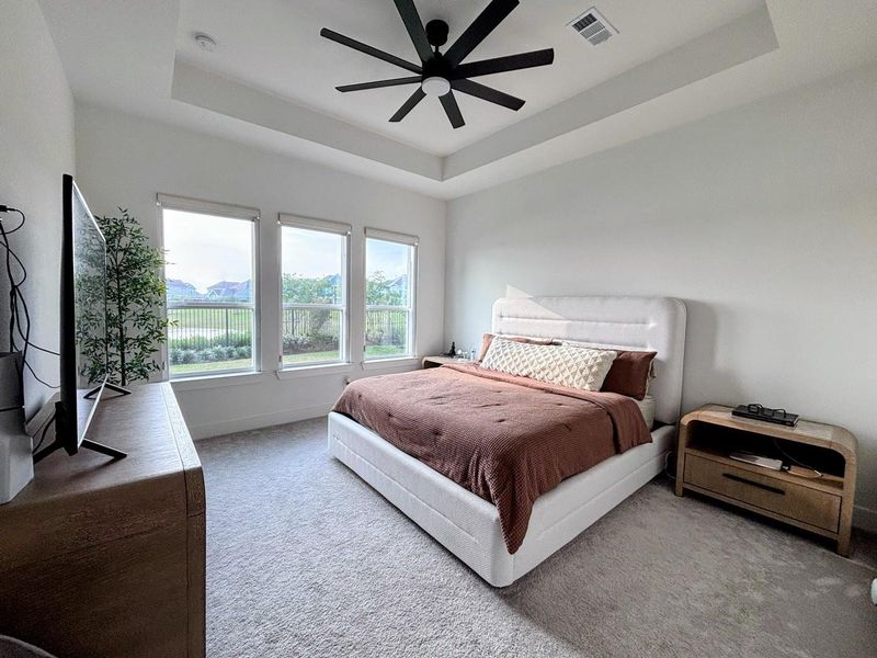 The master bedroom is spacious and bright, with a contemporary design. It has a ceiling fan, multiple windows offering natural light and a view, and is complemented by neutral tones and modern furnishings.