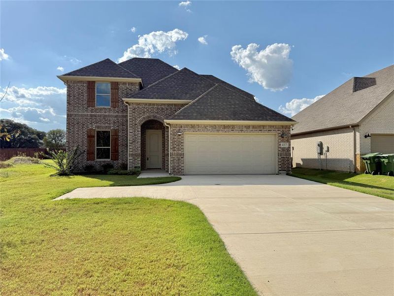 French provincial home with brick siding, a shingled roof, a front yard, concrete driveway, and an attached garage