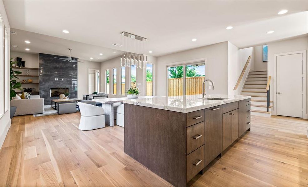 Kitchen featuring light wood-type flooring, a kitchen island with sink, recessed lighting, dark brown cabinetry, and a fireplace Kitchen featuring light wood-type flooring, a kitchen island with sink, recessed lighting, dark brown cabinetry, and a fireplace