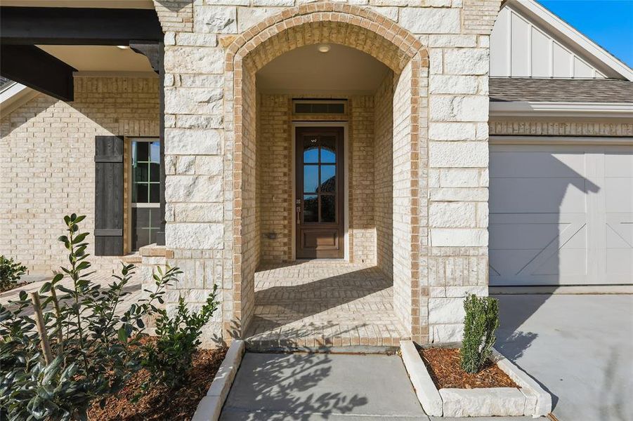 Property entrance featuring brick siding, stone siding, a garage, a shingled roof, and board and batten siding Property entrance featuring brick siding, stone siding, a garage, a shingled roof, and board and batten siding
