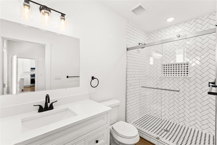Bathroom featuring a glass-enclosed shower with herringbone tile surround, a built-in shower niche with decorative tile, and a patterned tile shower pan