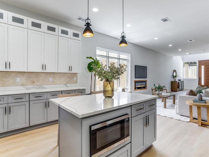 Contemporary kitchen featuring a two-tone cabinetry design with white upper and gray lower cabinets, a central island with a built-in microwave, white stone countertops, and wood-finish flooring Contemporary kitchen featuring a two-tone cabinetry design with white upper and gray lower cabinets, a central island with a built-in microwave, white stone countertops, and wood-finish flooring