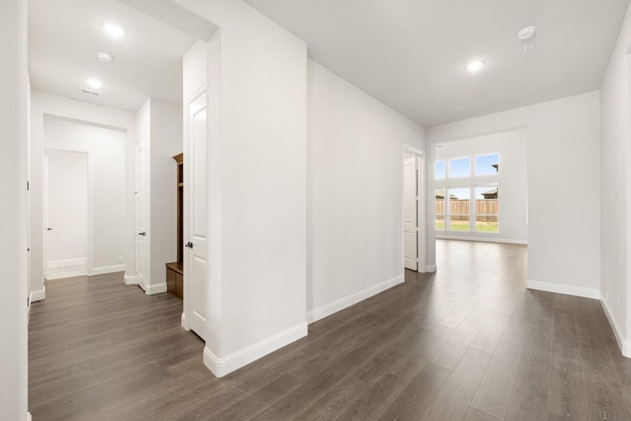Open living area with dark hardwood floors, white walls, and a hallway leading to additional rooms Open living area with dark hardwood floors, white walls, and a hallway leading to additional rooms