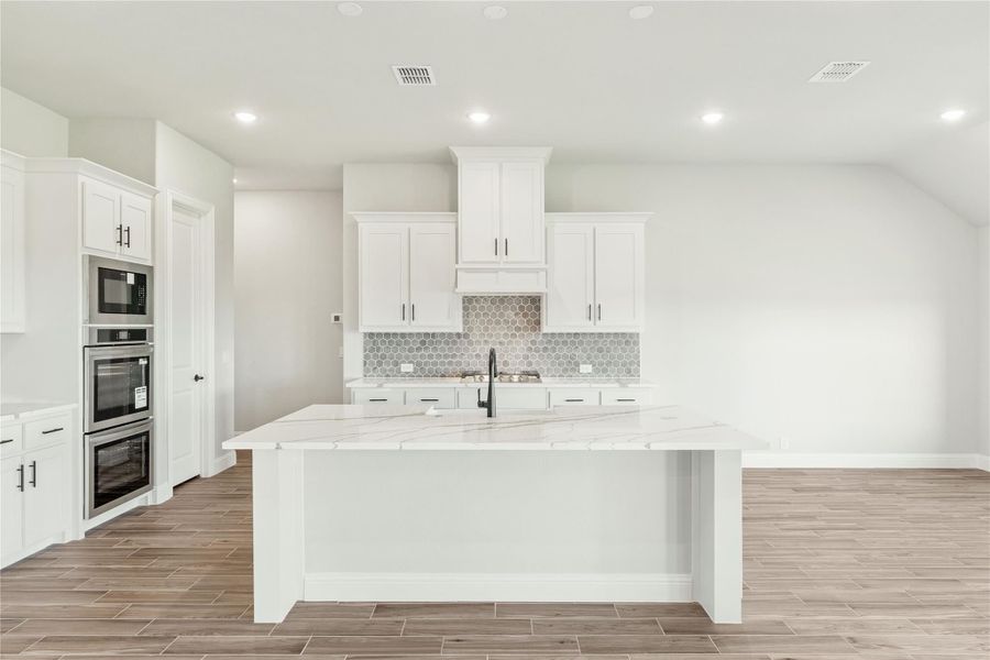 White kitchen with large island, marble countertops, stainless steel appliances, and hexagon tile backsplash White kitchen with large island, marble countertops, stainless steel appliances, and hexagon tile backsplash