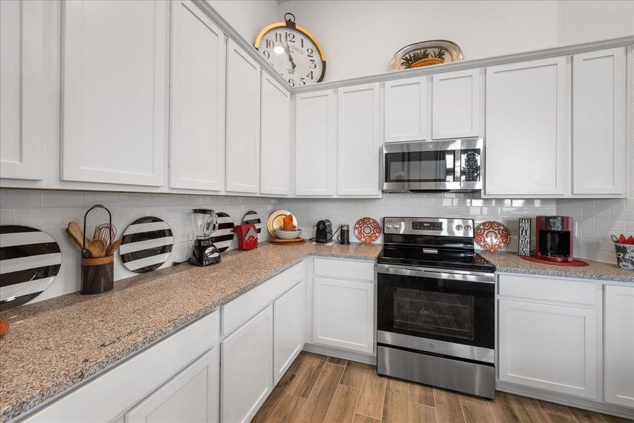 Kitchen with stainless steel appliances, white cabinetry, light wood-style flooring, and light stone counters Kitchen with stainless steel appliances, white cabinetry, light wood-style flooring, and light stone counters