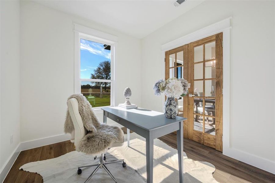 Bright and versatile office or flex space bathed in natural light from oversized window overlooking serene views of front. Elegant French doors with rustic wood finish provide privacy while maintaining visual connection to formal dining and foyer.