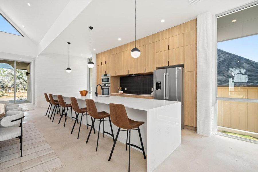 Kitchen featuring a breakfast bar, a spacious island, decorative light fixtures, light wood finish cabinetry, and light stone counters