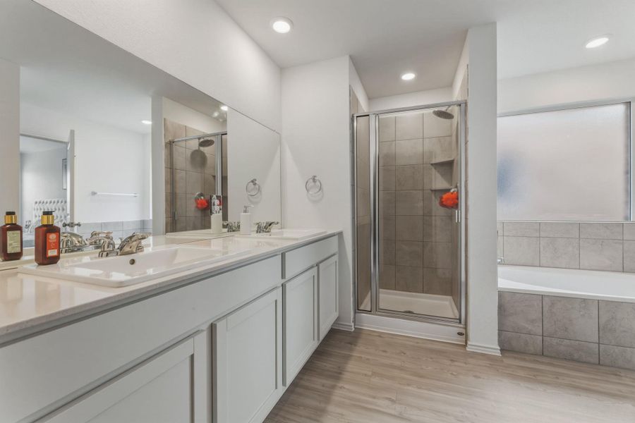 Bathroom featuring a double vanity with white countertops, a tiled walk-in shower with a glass enclosure, and a tiled bathtub