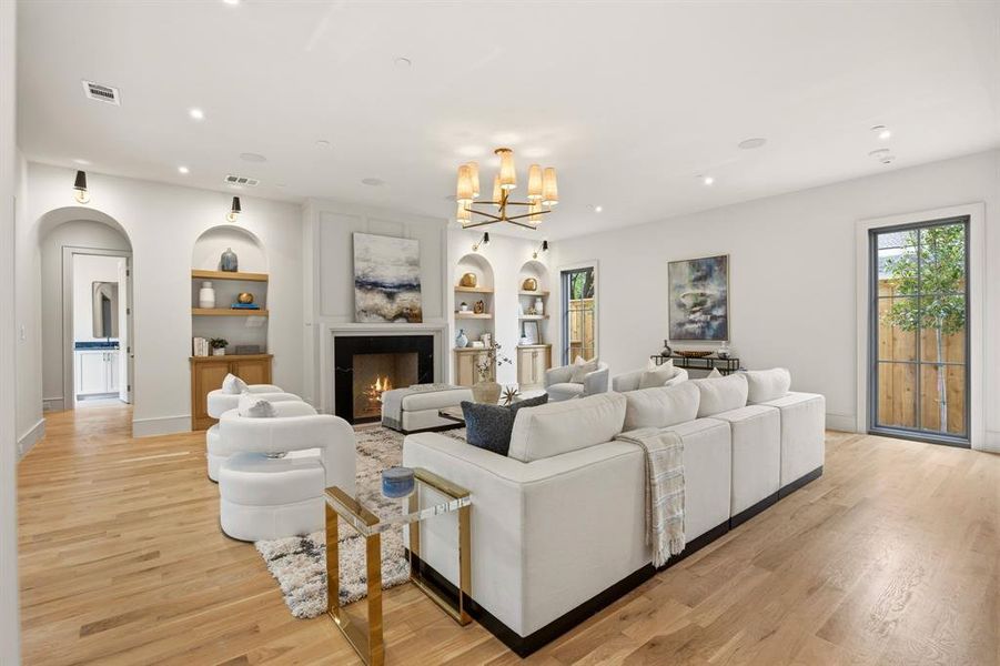 Spacious living area featuring wood-finish flooring, a central fireplace with a dark surround, and a decorative mantel Spacious living area featuring wood-finish flooring, a central fireplace with a dark surround, and a decorative mantel