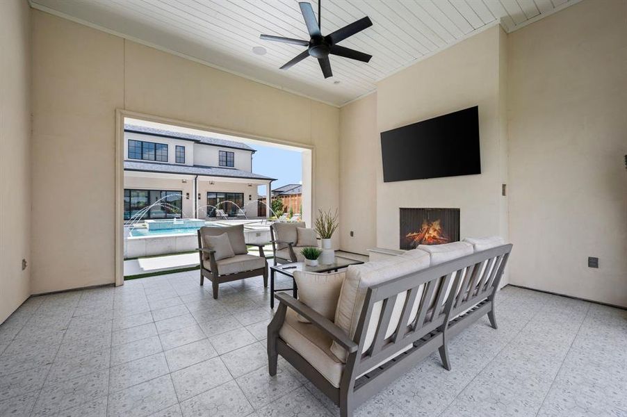 Living area with ornamental molding, a warm lit fireplace, a ceiling fan, a high ceiling, and light floors Living area with ornamental molding, a warm lit fireplace, a ceiling fan, a high ceiling, and light floors