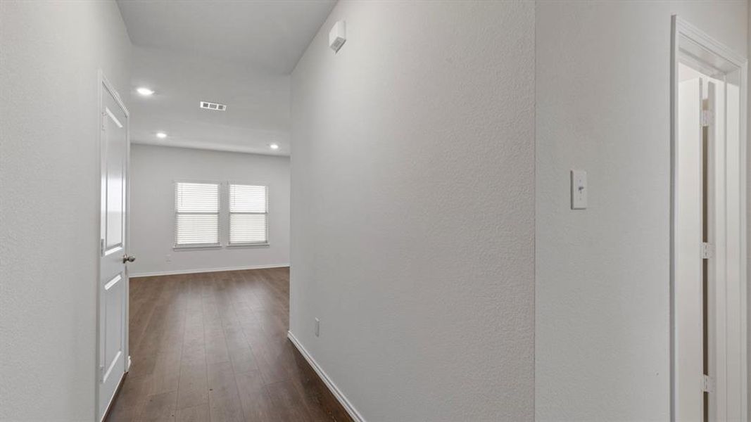 Hallway with wood-finish flooring extending into a bright room featuring two windows and recessed lighting
