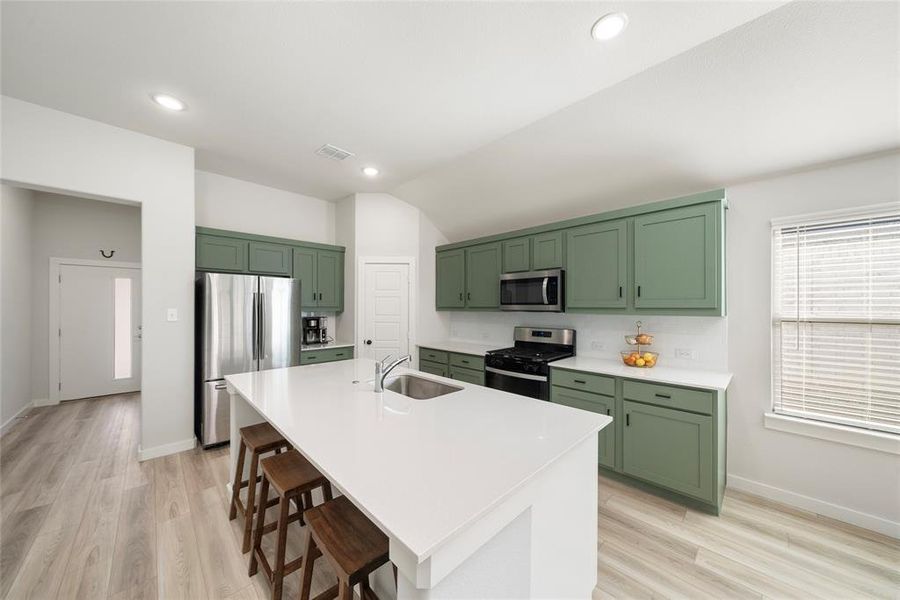 Kitchen featuring stainless steel appliances, green cabinets, sink, a center island with sink, and a breakfast bar area