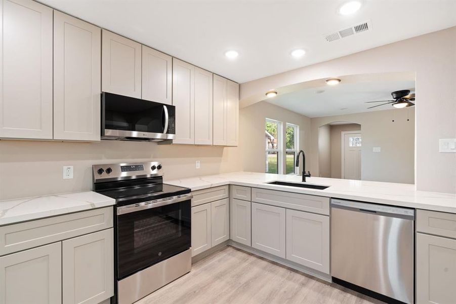 Kitchen with stainless steel appliances, light wood finished floors, light stone counters, ceiling fan, and recessed lighting
