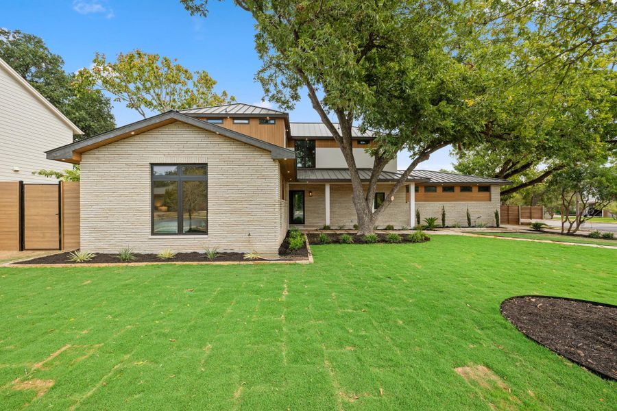 Mature trees shade a manicured green lawn leading to a modern stone and wood exterior.