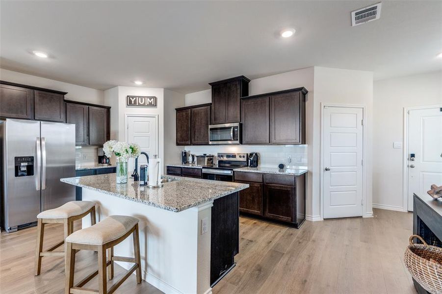 Kitchen featuring decorative backsplash, stainless steel appliances, dark brown cabinetry, light wood-style flooring, and recessed lighting Kitchen featuring decorative backsplash, stainless steel appliances, dark brown cabinetry, light wood-style flooring, and recessed lighting
