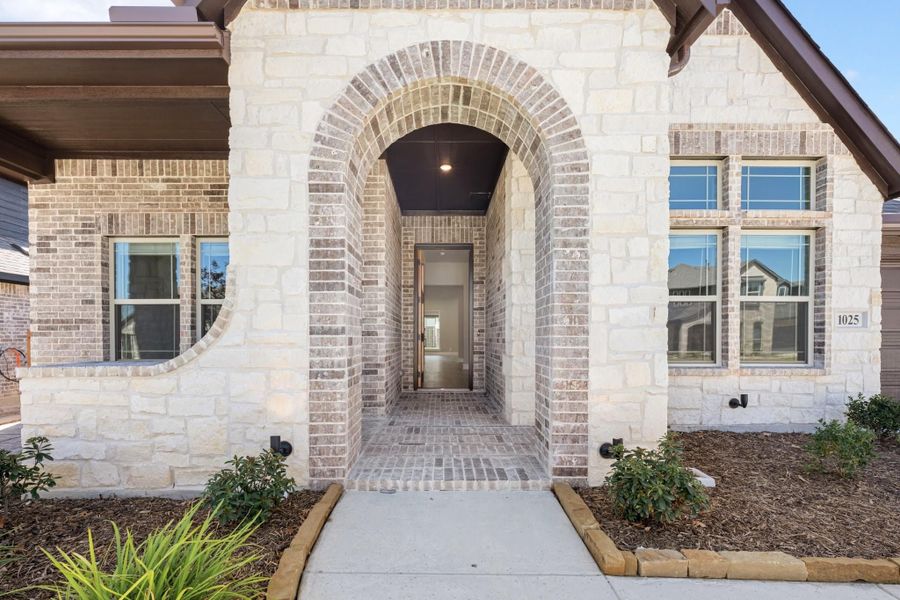 Home entrance with arched brick and stone surround, covered entryway, and open front door with landscaped walkway.