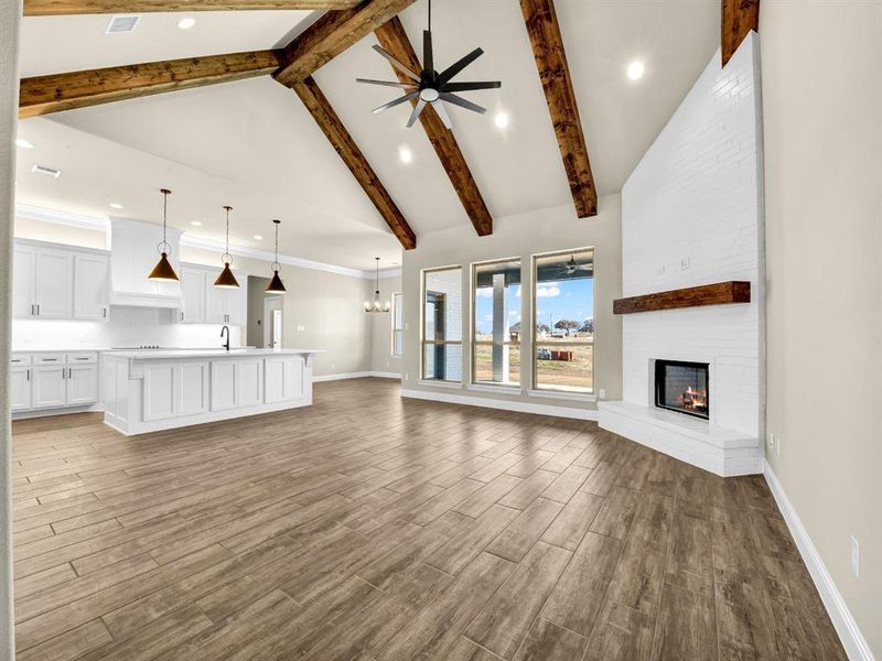 Unfurnished living room featuring sink, beamed ceiling, a large fireplace, ceiling fan with notable chandelier, and high vaulted ceiling