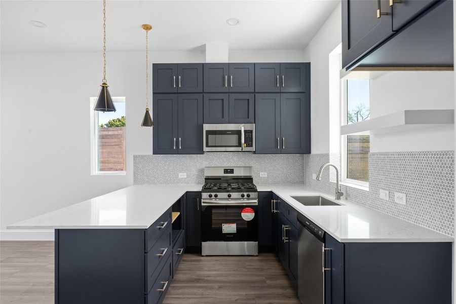 Kitchen featuring stainless steel appliances, light stone counters, a peninsula, and hanging light fixtures Kitchen featuring stainless steel appliances, light stone counters, a peninsula, and hanging light fixtures