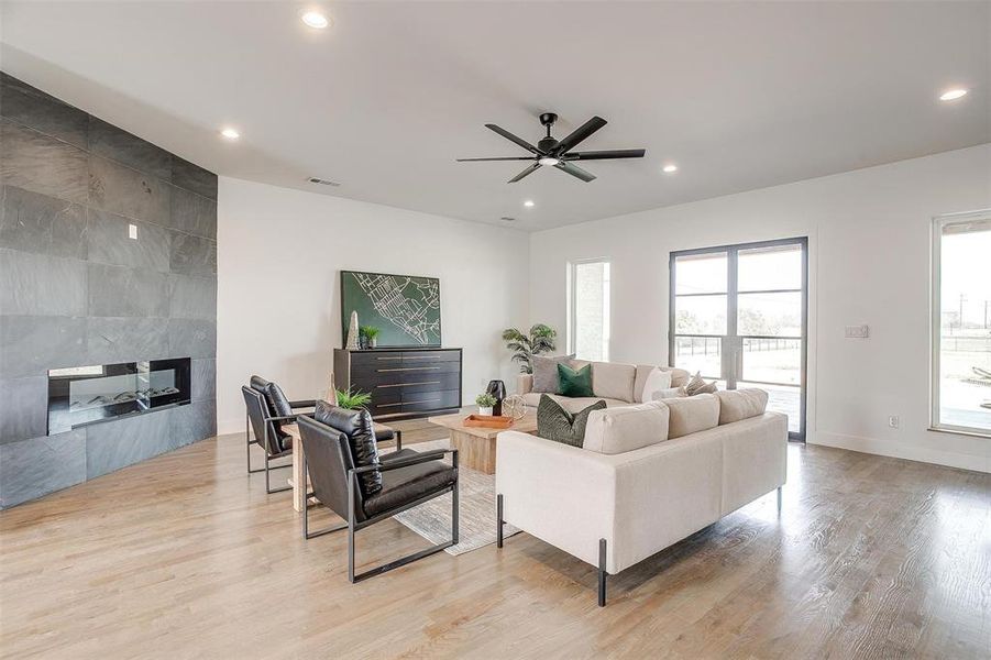 Living room with baseboards, visible vents, a tiled fireplace, wood finished floors, and recessed lighting