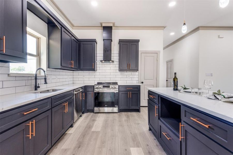 Kitchen with sink, hanging light fixtures, light hardwood / wood-style flooring, backsplash, and appliances with stainless steel finishes