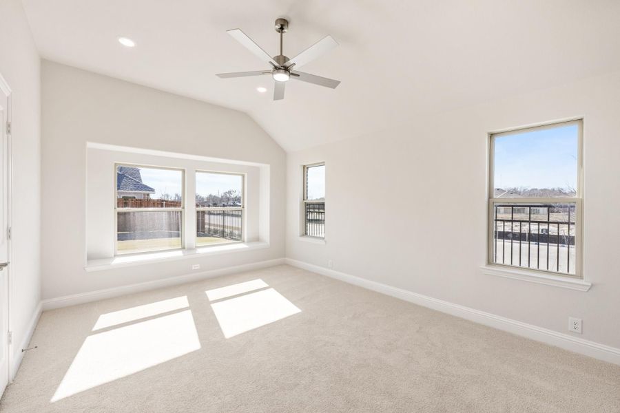 Empty bedroom with vaulted ceiling, ceiling fan, carpet flooring, and multiple windows with natural light Empty bedroom with vaulted ceiling, ceiling fan, carpet flooring, and multiple windows with natural light