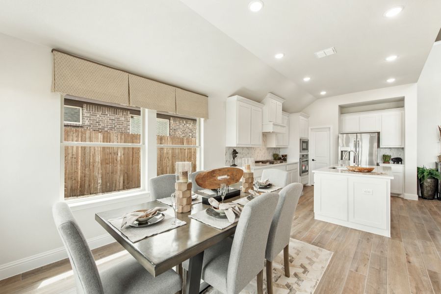 Open dining area with set table and chairs, connected to white kitchen with island and hardwood floors