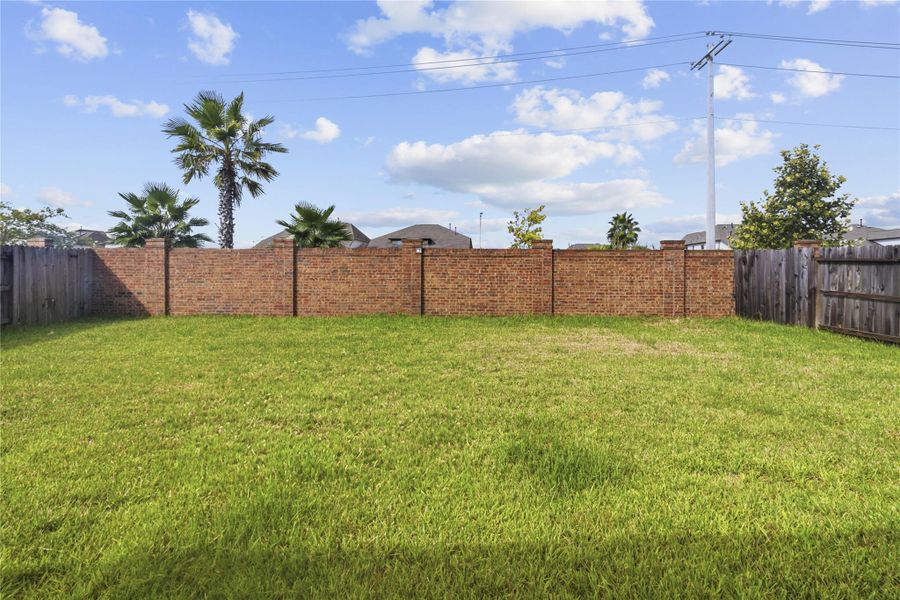 Spacious backyard with lush green grass, bordered by a combination of brick and wooden fencing, enhanced by palm trees for a touch of tropical flair. Spacious backyard with lush green grass, bordered by a combination of brick and wooden fencing, enhanced by palm trees for a touch of tropical flair.
