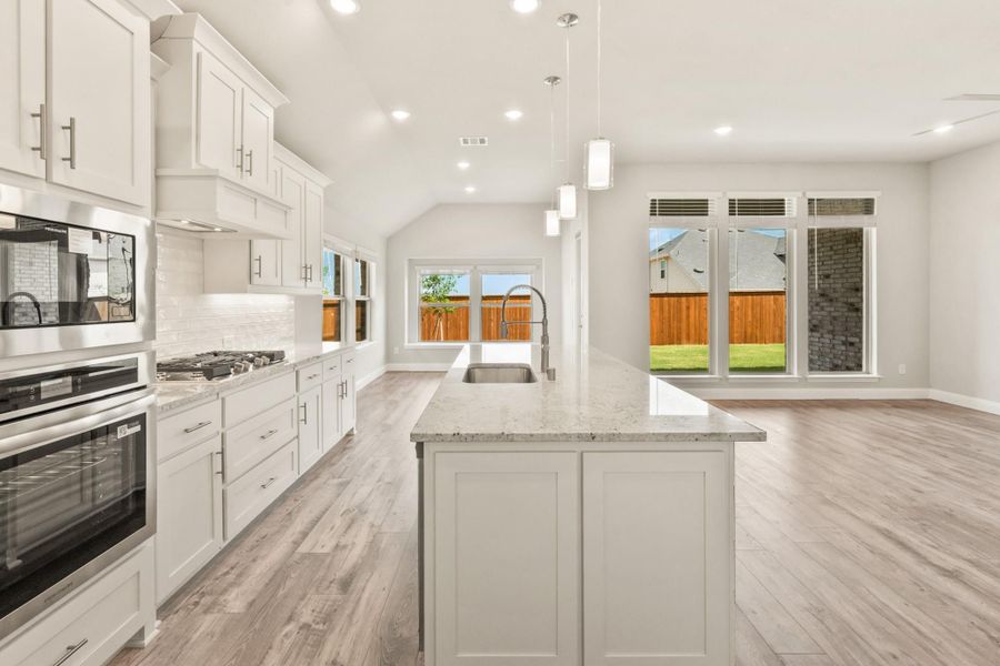 Open kitchen with white cabinets, granite island with sink, stainless appliances, and light wood floors Open kitchen with white cabinets, granite island with sink, stainless appliances, and light wood floors