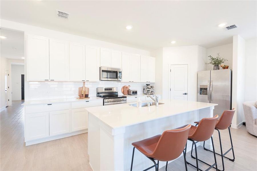 Kitchen featuring light wood-type flooring, stainless steel appliances, a kitchen bar, white cabinets, and a kitchen island with sink Kitchen featuring light wood-type flooring, stainless steel appliances, a kitchen bar, white cabinets, and a kitchen island with sink
