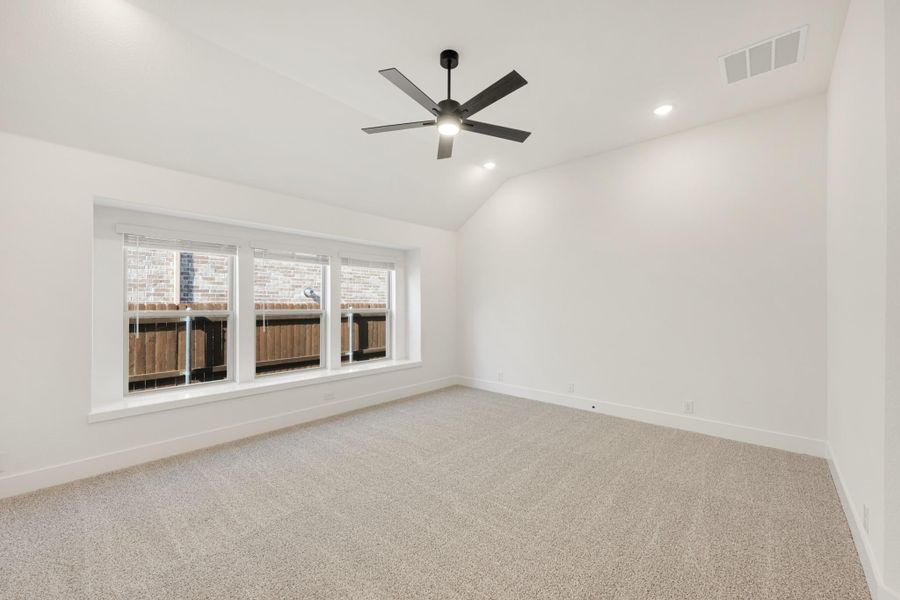 Empty bedroom with vaulted ceiling, black ceiling fan, carpet flooring, and triple windows Empty bedroom with vaulted ceiling, black ceiling fan, carpet flooring, and triple windows