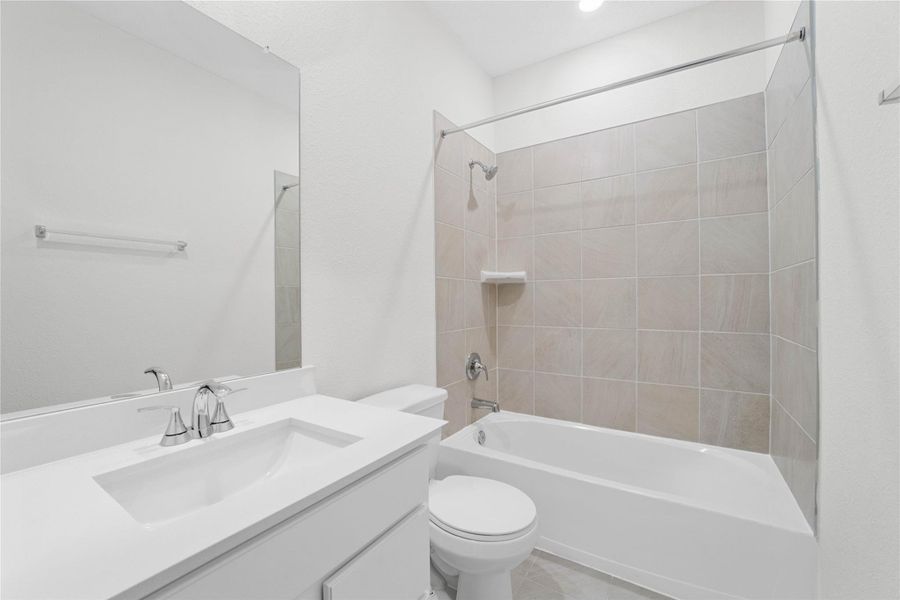 The secondary bathroom showcases tile flooring, a bath/shower combo with Daltile tile surround, a vanity with a stunning light countertop, a mirror, sleek fixtures, and contemporary finishes throughout.