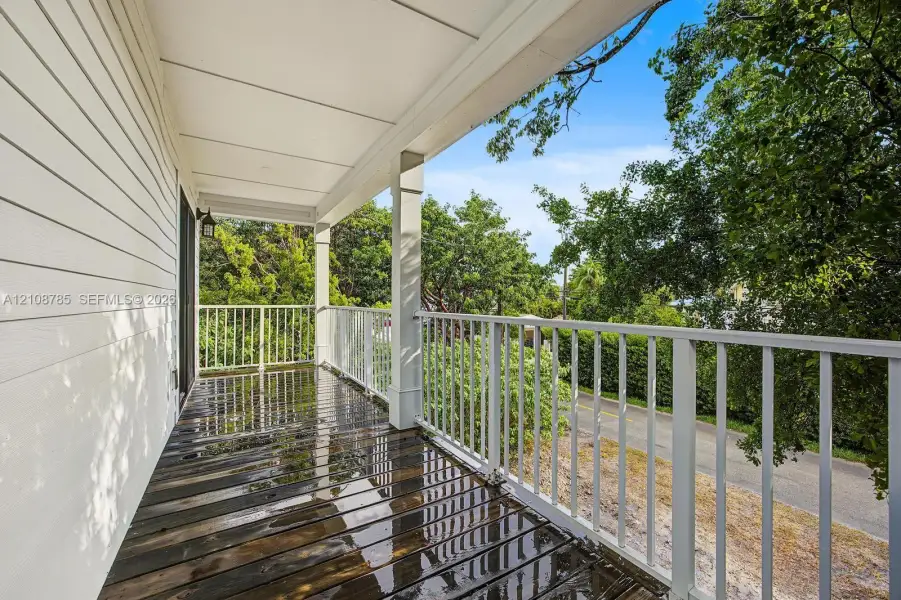 Covered exterior balcony featuring wood-plank flooring, white structural columns, and white vertical-bar railings Covered exterior balcony featuring wood-plank flooring, white structural columns, and white vertical-bar railings