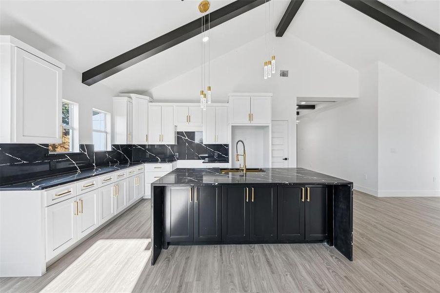 Kitchen with dark cabinets, a spacious island, white cabinets, high vaulted ceiling, and decorative light fixtures Kitchen with dark cabinets, a spacious island, white cabinets, high vaulted ceiling, and decorative light fixtures