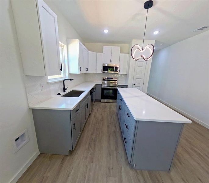 Kitchen with gray cabinetry, white cabinets, appliances with stainless steel finishes, backsplash, and light wood-style flooring Kitchen with gray cabinetry, white cabinets, appliances with stainless steel finishes, backsplash, and light wood-style flooring