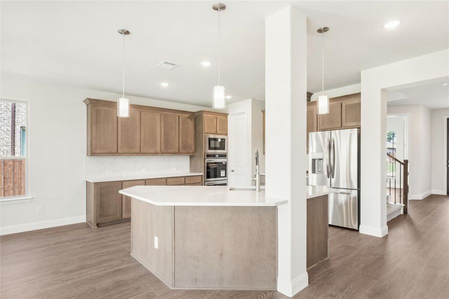 Open kitchen with tan wood cabinets, large island, stainless steel appliances, and hardwood floors