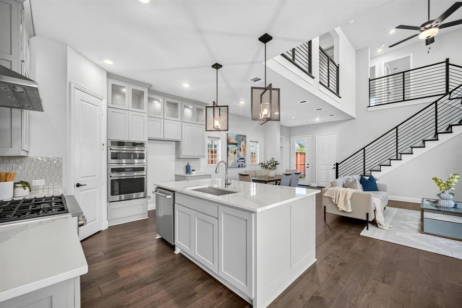 Open-concept kitchen and living area featuring wood-finish flooring, a kitchen island with a built-in sink, stainless steel appliances, and light-toned cabinetry