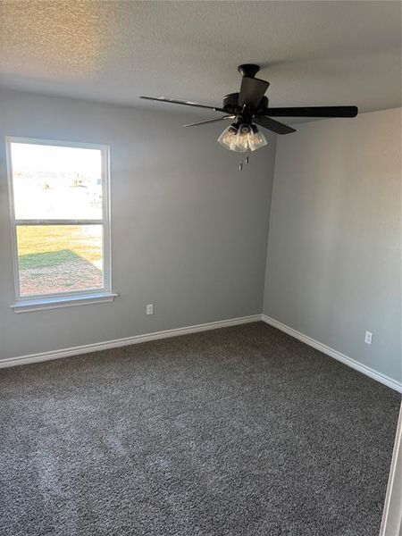 Unfurnished room with ceiling fan, a textured ceiling, and dark colored carpet