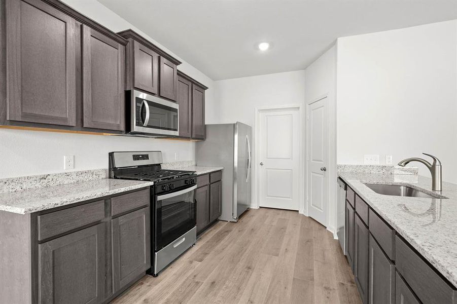 Kitchen with appliances with stainless steel finishes, light stone counters, light wood finished floors, dark brown cabinetry, and a peninsula