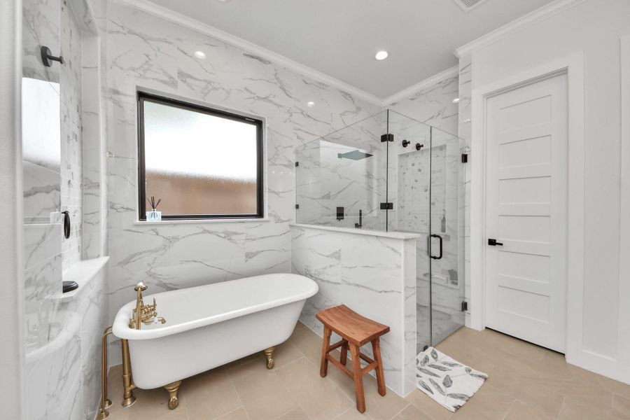 This elegant bathroom features a freestanding clawfoot tub, glass-enclosed shower, and marble-patterned walls. It offers a modern, spa-like atmosphere with a large window for natural light and a sleek design.