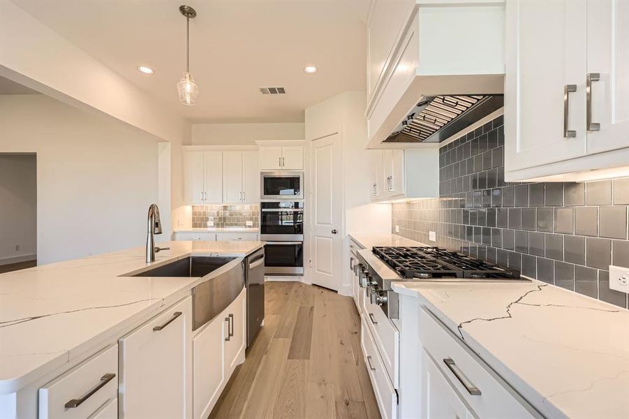 Kitchen featuring white cabinetry, light stone counters, light hardwood / wood-style flooring, decorative light fixtures, and custom range hood