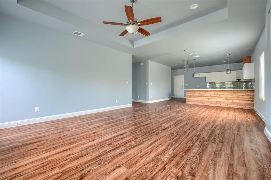 Unfurnished living room with a raised ceiling, sink, light wood-type flooring, and ceiling fan