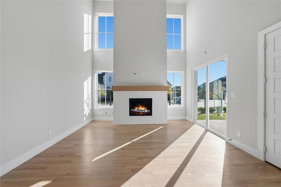 Unfurnished living room featuring a towering ceiling, wood finished floors, and a brick fireplace