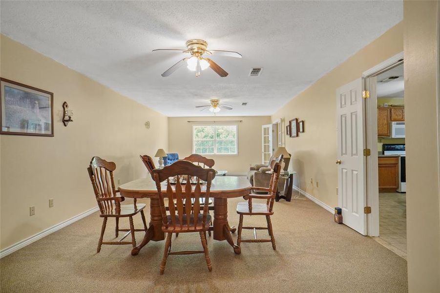 Dining room featuring ceiling fan, light colored carpet, and a textured ceiling