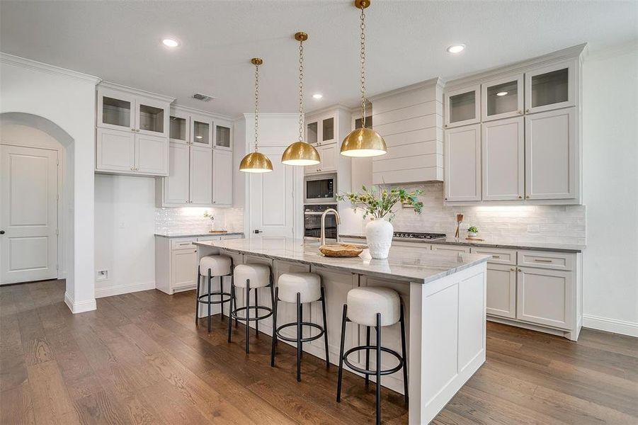 Kitchen featuring a large island, Quartzite countertops, gold hardware, decorative light fixtures, custom cabinetry to the ceiling, gas cooktop, double oven and walk in pantry