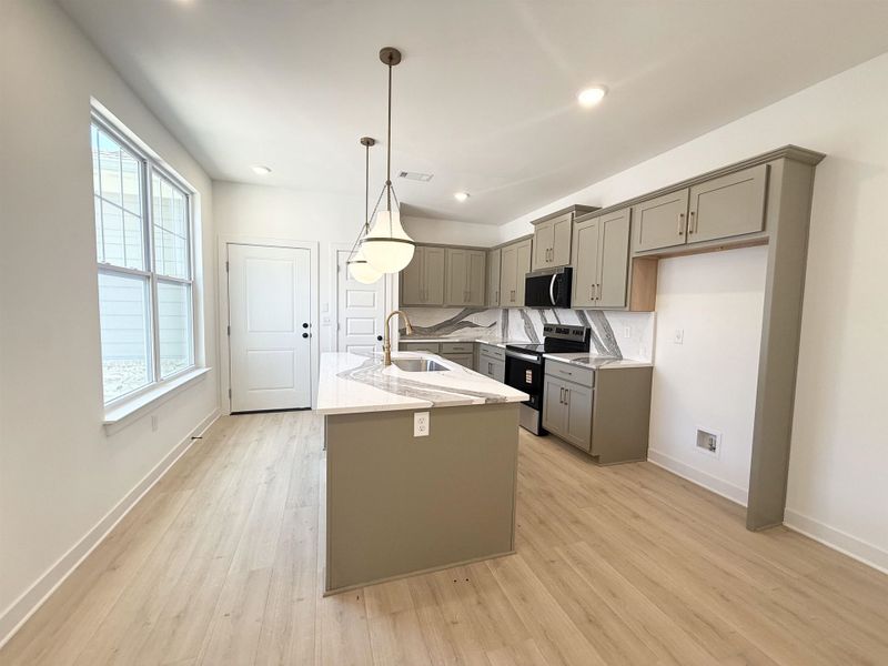 Kitchen with gray cabinetry, stainless steel appliances, light stone counters, a center island with sink, and light wood finished floors