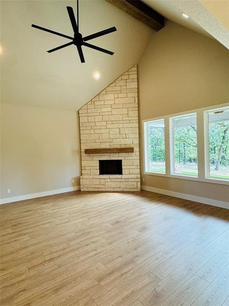 Unfurnished living room featuring a fireplace, high vaulted ceiling, beam ceiling, ceiling fan, and light wood finished floors Unfurnished living room featuring a fireplace, high vaulted ceiling, beam ceiling, ceiling fan, and light wood finished floors