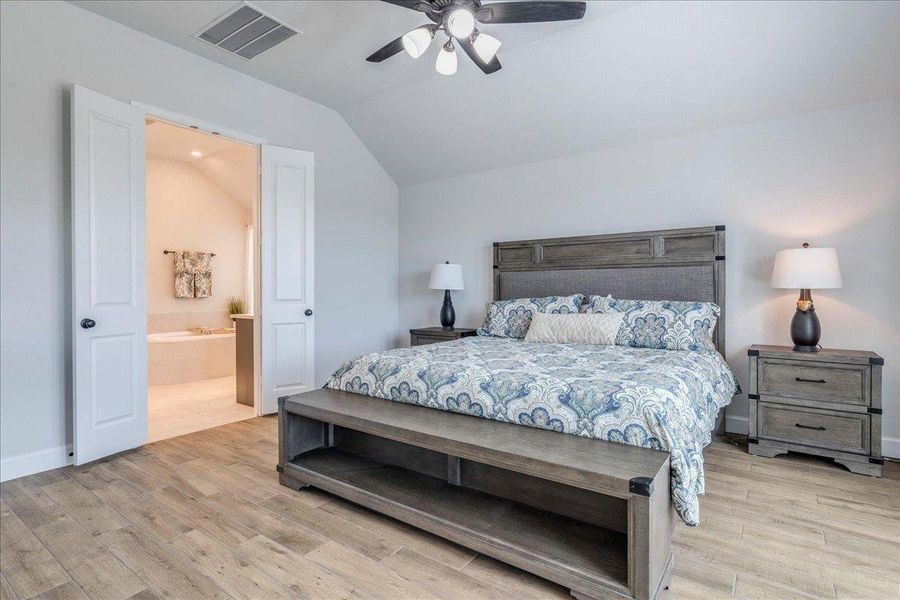 Bedroom with vaulted ceiling, light wood-style floors, ceiling fan, and ensuite bathroom
