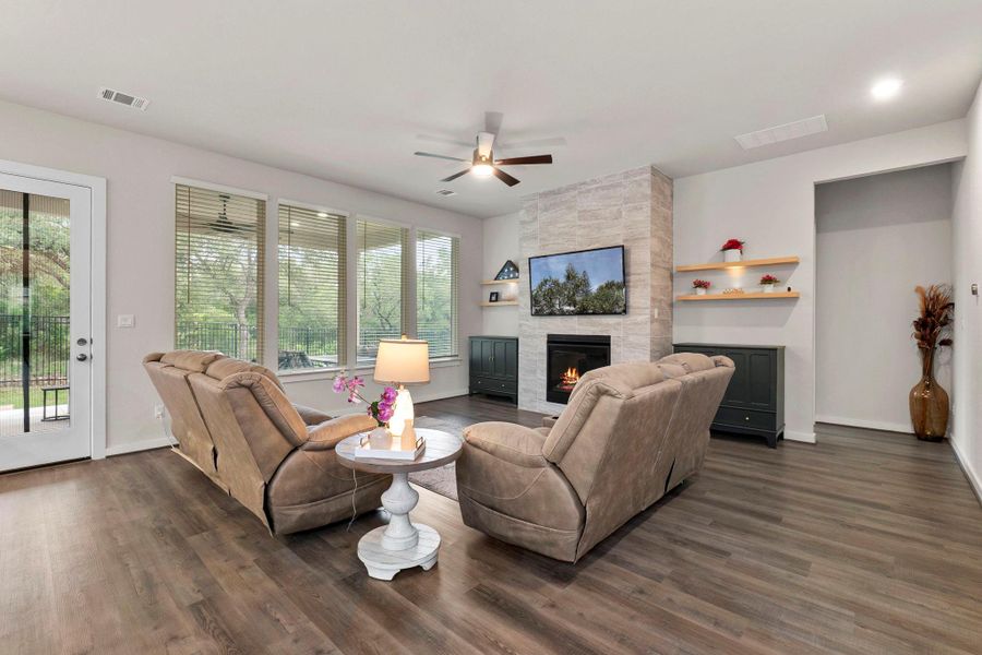 Living area featuring wood-finish flooring, a stone-accented fireplace, a ceiling fan, and multiple windows with blinds