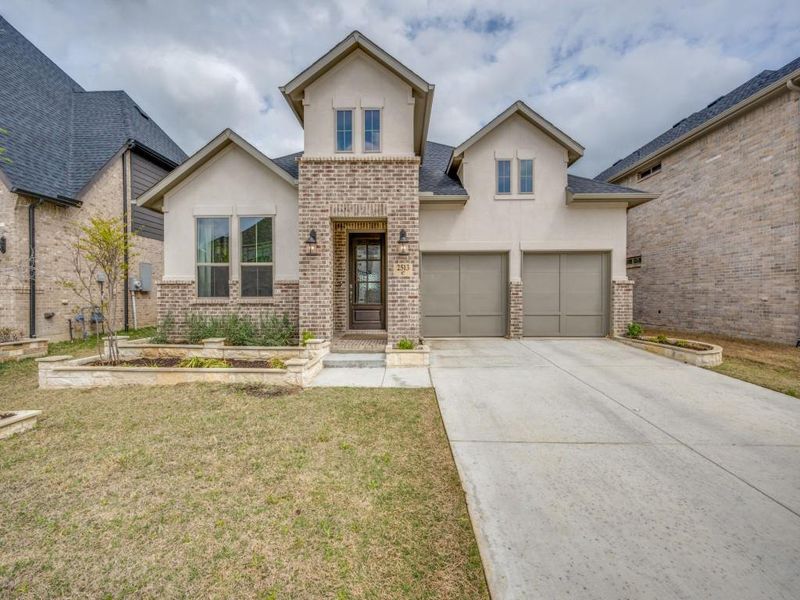 View of front facade with stucco siding, driveway, a front lawn, and brick siding