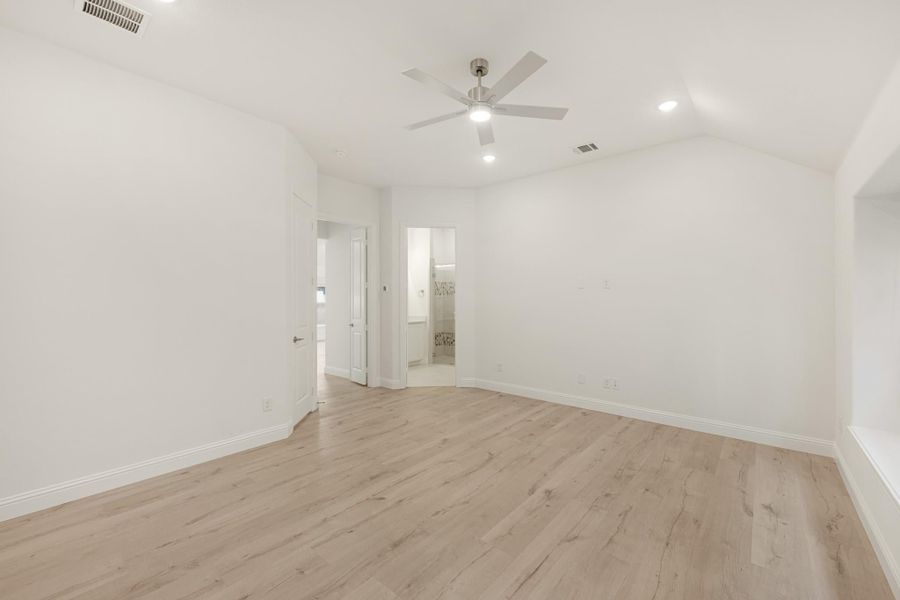 Empty bedroom with vaulted ceiling, ceiling fan, light wood floors, and ensuite bathroom doorway